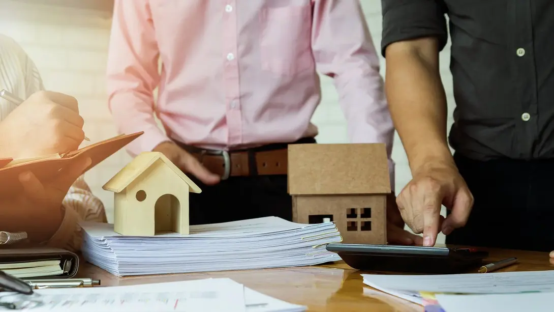Hausbaukosten gemeinsam kalkulieren Personen kalkulieren die Hausbaukosten neben Unterlagen und Hausmodellen