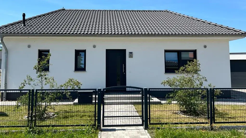 Moderner Bungalow mit Vorgarten Moderner Bungalow mit Walmdach, weißer Fassade, Vorgarten und eingezäuntem Grundstück.