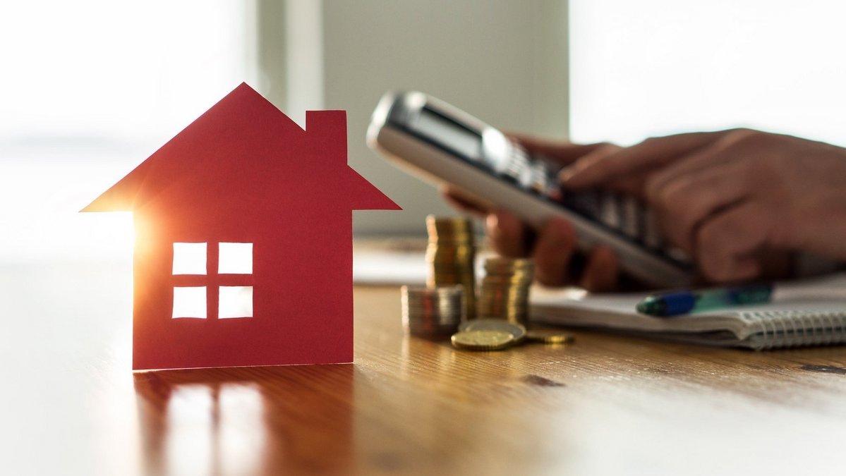 Haus-Symbol mit Münzen und Taschenrechner zur Planung von Eigenkapital und Baufinanzierung