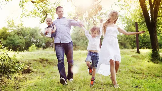 Familienleben im Grünen Familie mit zwei Kindern läuft gemeinsam durch eine grüne, sonnige Naturlandschaft.