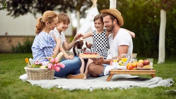 Familie picknickt mit Kindern und Hund im Garten