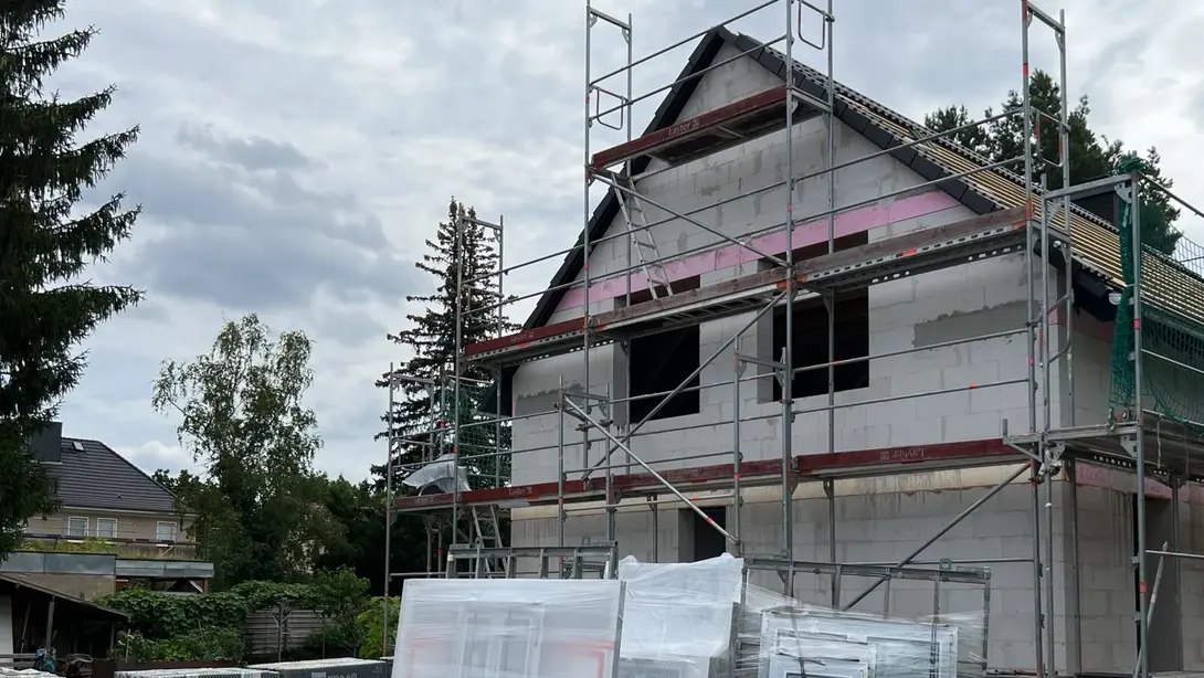 Einfamilienhaus im Rohbau Einfamilienhaus im Rohbau mit Gerüst, Satteldach und bereitliegenden Baumaterialien