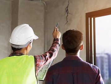Bauleiter und Bauherr begutachten eine Innenwand im Rohbau eines Hauses.