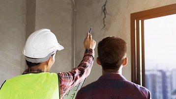 Bauherr und Fachmann prüfen einen Riss in der Wand bei der Bauabnahme