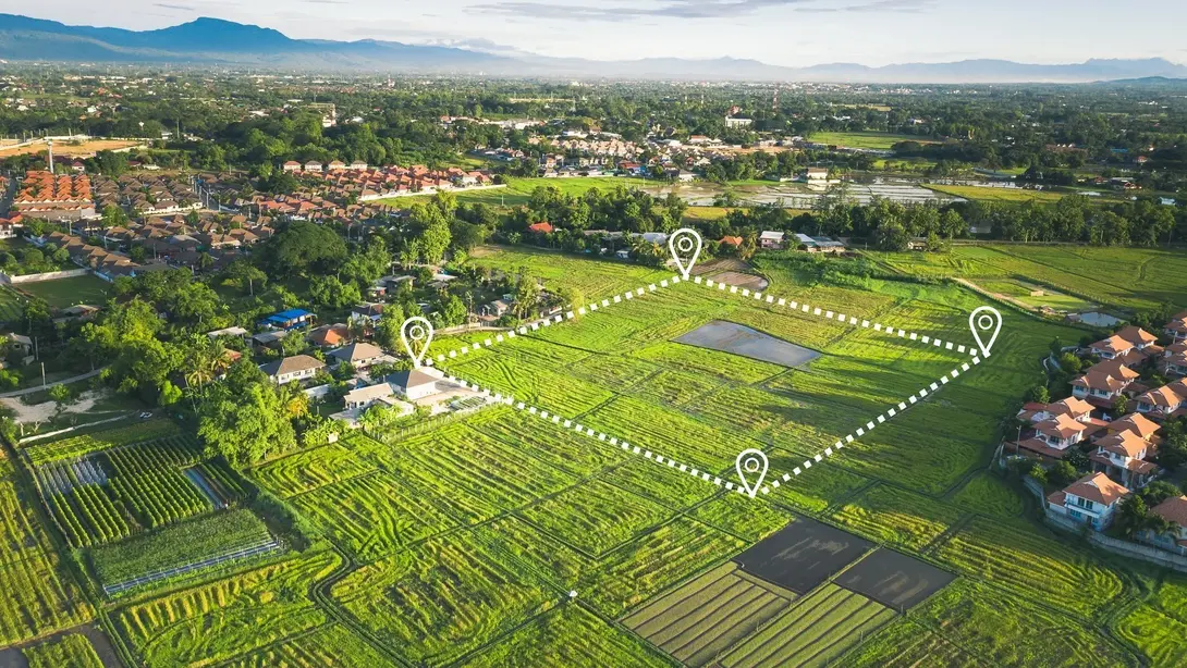 Luftaufnahme eines markierten Baugrundstücks am Rand eines Wohngebiets mit Feldern und weiter Landschaft.