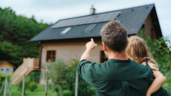 Vater mit Kind blickt auf ein modernes Einfamilienhaus mit Photovoltaikanlage