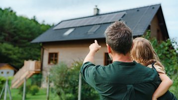 Vater mit Kind blickt auf ein modernes Einfamilienhaus mit Photovoltaikanlage