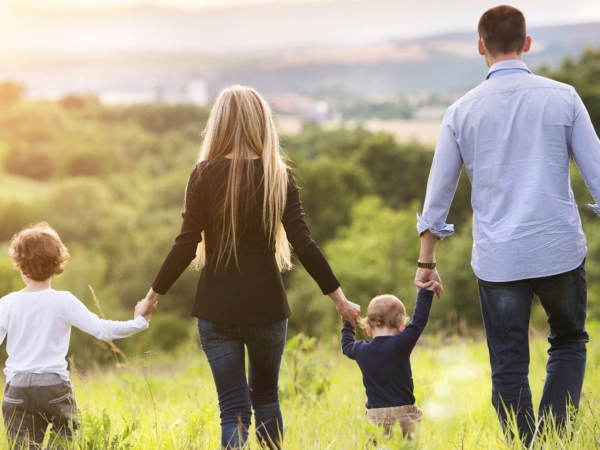 Familienleben im Grünen Familie mit zwei Kindern spaziert über eine Wiese und blickt in eine grüne Landschaft.
