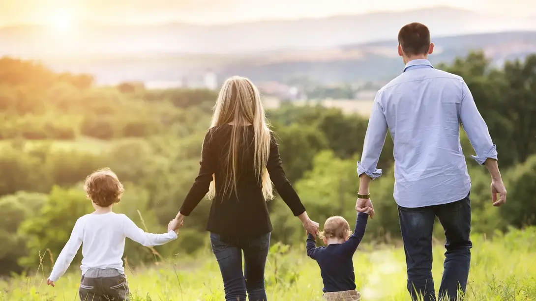 Familie mit zwei Kindern läuft über eine Wiese und blickt in eine grüne Landschaft.