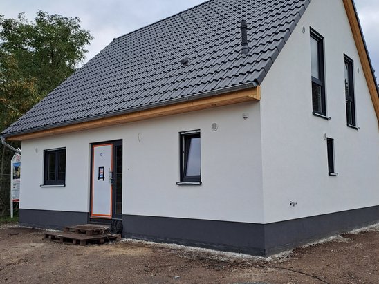 Weißes Einfamilienhaus mit Satteldach, dunklen Dachziegeln und modernen Fenstern während der abschließenden Bauphase.