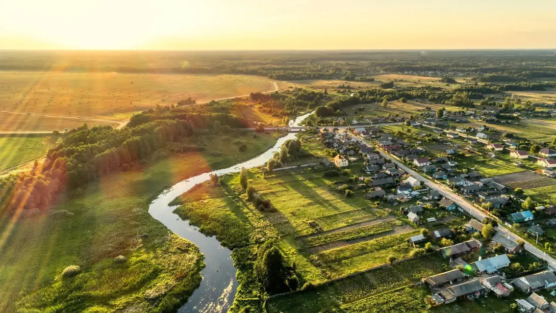 Luftaufnahme einer ländlichen Wohnlage mit Fluss, Feldern und Häusern bei Sonnenuntergang.
