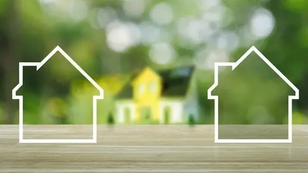 Das passende Haus für Ihre Wünsche finden Zwei weiße Hausumrisse vor einem unscharfen Hausmodell im Grünen