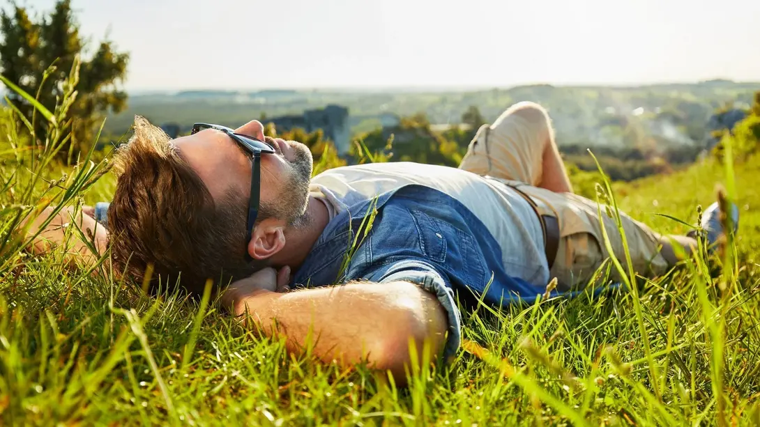 Entspanntes Leben inmitten der Natur Entspannter Mann liegt bei Sonnenschein auf einer grünen Wiese