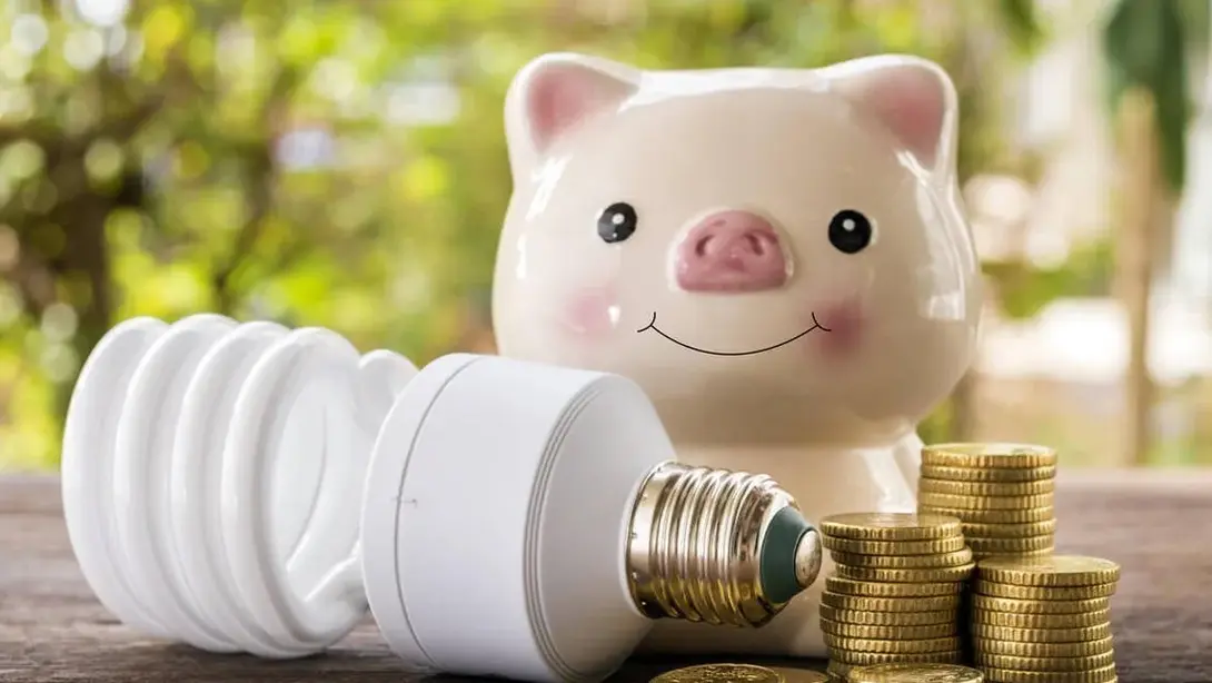 Energiesparlampe, Sparschwein und Münzen als Symbole für geringere Energiekosten