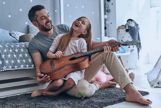 Haus-Vater-Tochter-Wohnen-Serie-4-23 Junger Vater bringt seiner Tochter das Gitarre spielen bei.