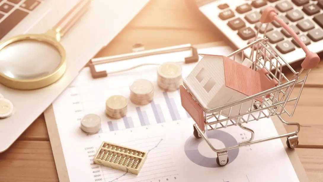 Kosten und Finanzierung beim Hausbau planen Einkaufswagen mit Miniaturhaus, Münzen, Taschenrechner und Finanzdiagrammen zur Hausbauplanung