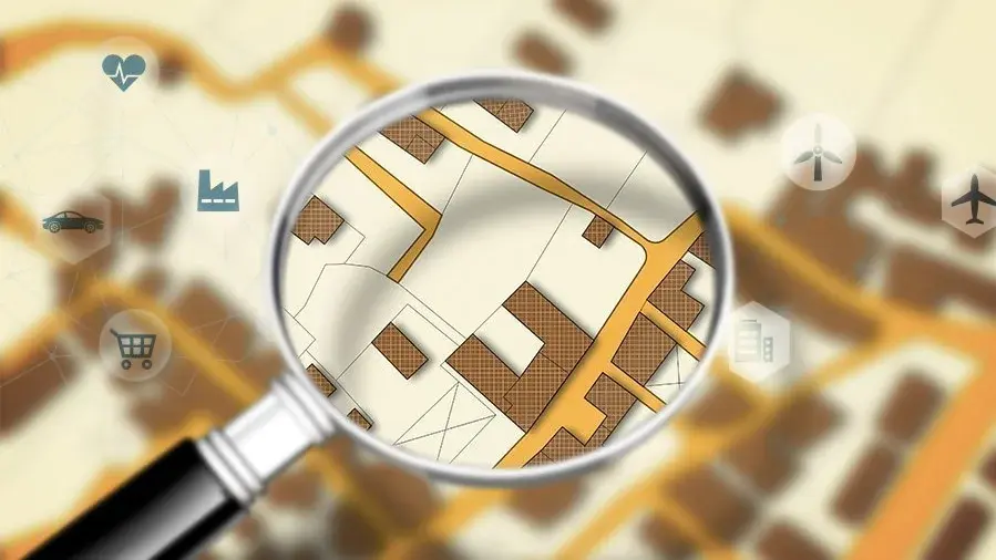 Grundstückssuche mit Standortanalyse Lupe über einem Stadtplan zur Suche nach Grundstücken und passenden Wohnlagen.